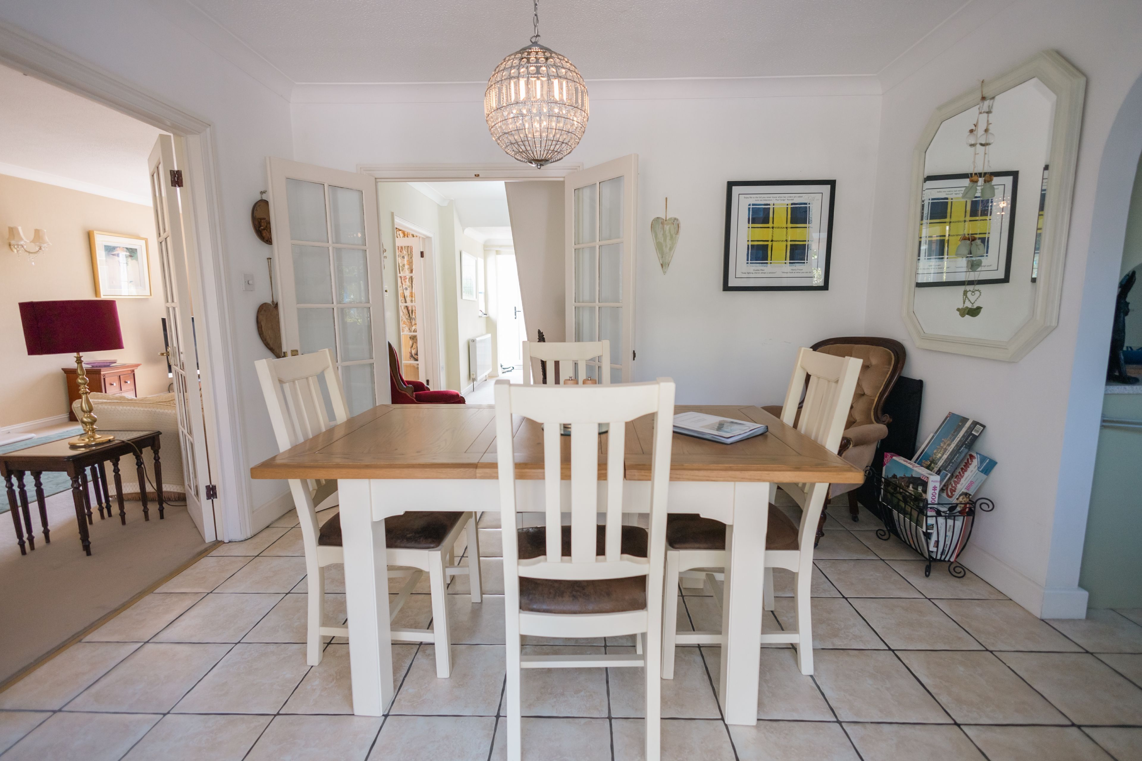 A dining area with a wooden table and white chairs, a chandelier, and a magazine rack.