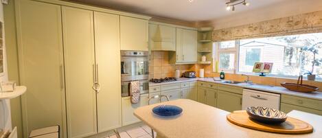A kitchen with light green cabinets, a central island, and a window with a view of the outdoors.