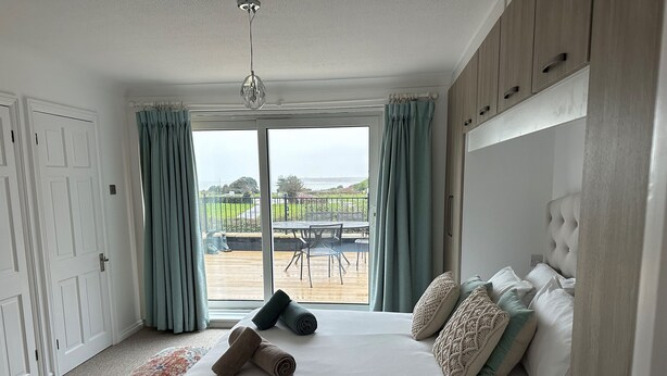 Un dormitorio con una cama grande, vistas al exterior y un balcón con mobiliario.