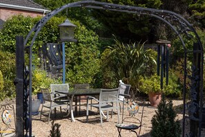 A garden patio with a table and chairs, surrounded by potted plants and a decorative metal archway. - 'Raggleswood' - a seaside home on Friars Cliff, Mudeford (Christchurch)