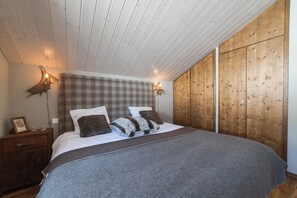 A bedroom with a bed, wooden walls, a headboard, bedside lamps, a nightstand, and a framed picture.
