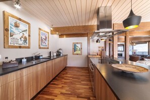 Une cuisine moderne avec des armoires en bois, un comptoir noir et un îlot central. Deux affiches encadrées ornent le mur, ainsi qu’une hotte de cuisinière en acier inoxydable et un luminaire suspendu.
