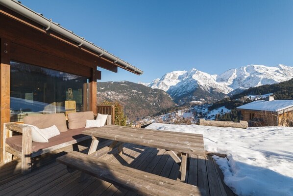 A wooden deck with a bench and a table, overlooking a snowy mountain landscape.