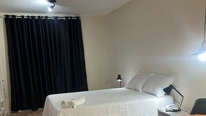 A neatly arranged bedroom with a bed, bedside table, lamp, and a small round table. - Ap Smart Hub  (Campinas)