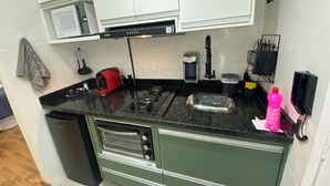 A compact kitchen with a gas stove, a built-in oven, a microwave, and a coffee maker. - Smart Business Flat (Campinas)