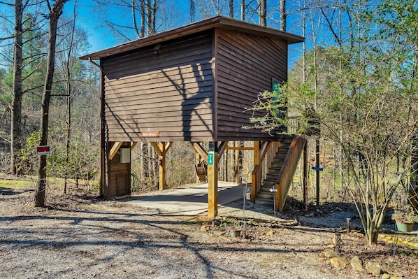A wooden cabin with a porch, surrounded by trees.