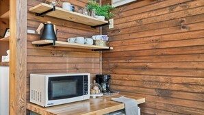 Eine Küche mit Mikrowelle, Kaffeemaschine und Holzregalen mit Geschirr.