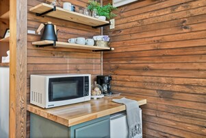 Una cocina con microondas, cafetera y repisas de madera con utensilios de cocina.