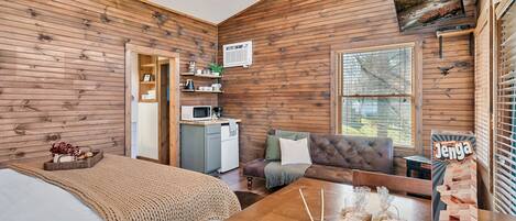 A cozy cabin interior with a wooden interior, a bed, a sofa, a dining table, and a kitchenette.