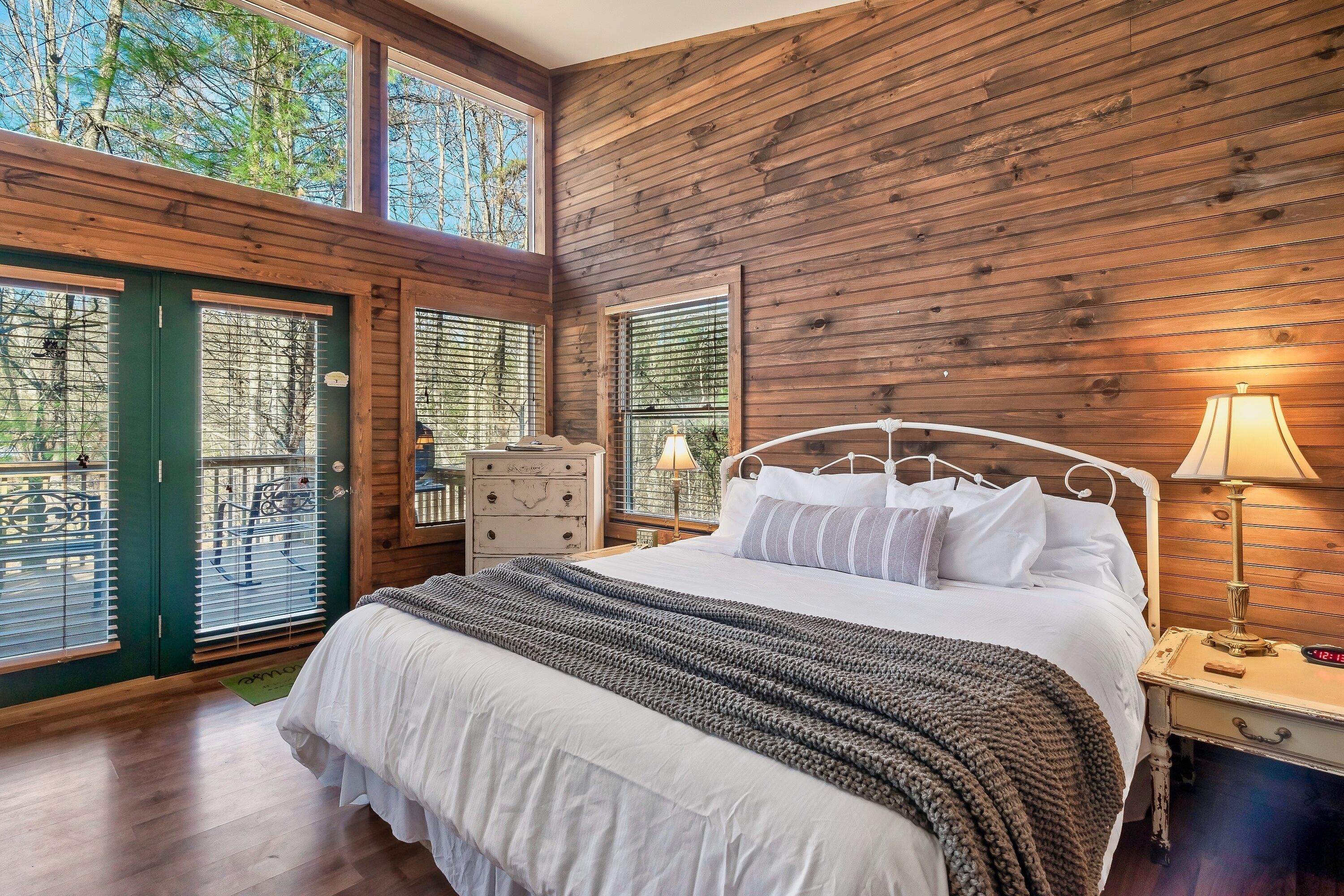 A bedroom with a wooden ceiling, a large bed with white bedding, a nightstand with a lamp, and a dresser.