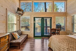 Interior acogedor de una cabaña con piso de madera, un sofá con un cojín floral, una cama con una colcha acolchada y un escritorio con una silla.