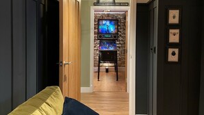 A room with a green couch, a wooden door, a stone wall, and a television in the background.
