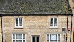 A stone building with a tiled roof, two windows on the ground floor, and a door.