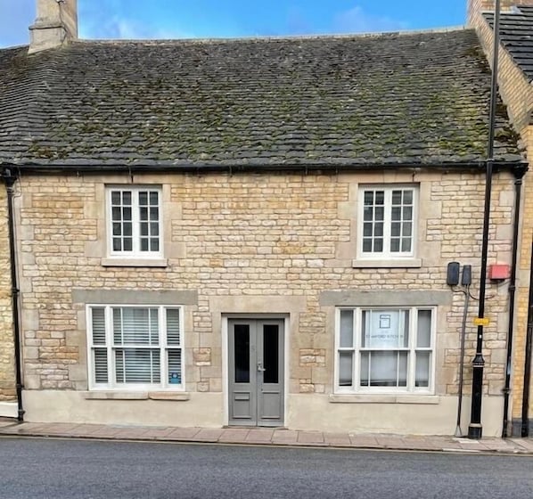 A stone building with a tiled roof, two windows on the ground floor, and a door.