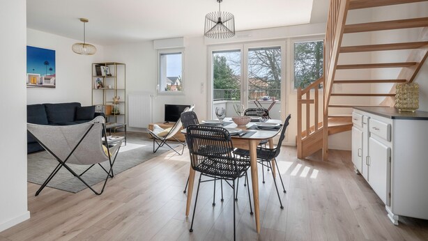 Ein moderner Wohnraum mit Essbereich, einer Couch, einem Bücherregal und einer Treppe.