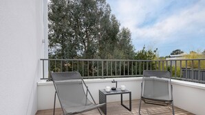 Ein Balkon mit zwei Stühlen und einem kleinen Tisch, mit Blick auf einen Garten und Bäume.