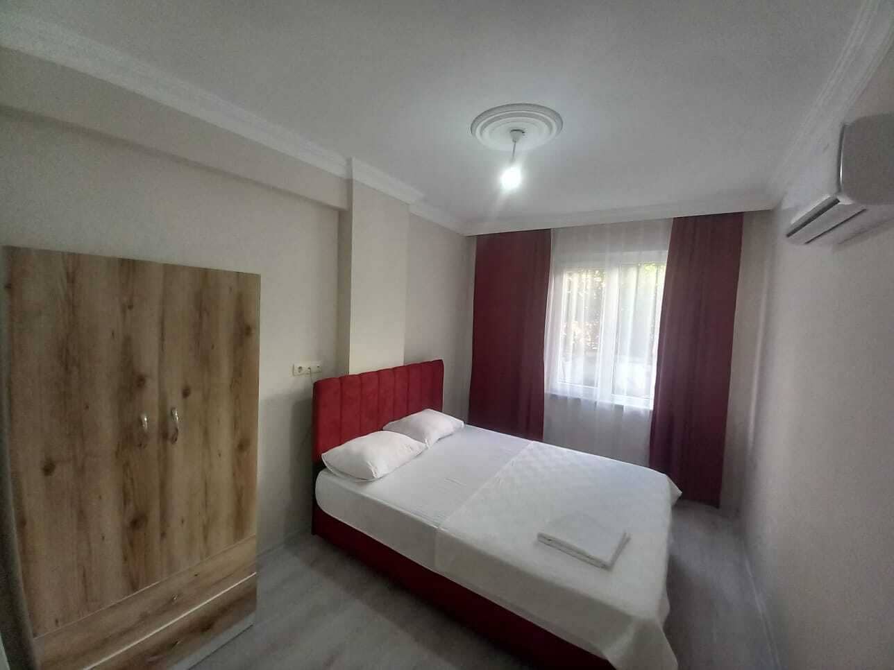 A bedroom with a wooden wardrobe, a bed with white bedding, and a ceiling light.
