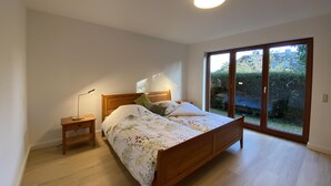 A bedroom with a wooden bed, a nightstand, a lamp, and a large sliding glass door leading to a garden. - Ferienwohnung (Kröppelshagen-Fahrendorf)