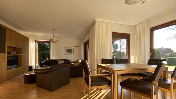 A modern living room with a wooden dining table and chairs, a sofa, and a television. - Ferienwohnung (Kröppelshagen-Fahrendorf)