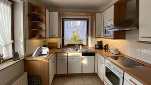 A modern kitchen with white cabinets, a dishwasher, an oven, and a window with curtains. - Ferienwohnung (Kröppelshagen-Fahrendorf)