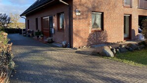 A two-story brick house with a paved driveway, a wooden door, and a small balcony. - Ferienwohnung (Kröppelshagen-Fahrendorf)