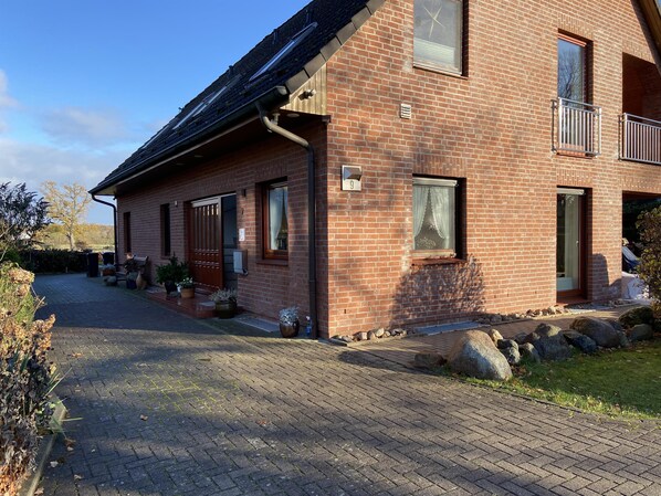 Ein zweistöckiges Backsteinhhaus mit gepflasterter Auffahrt, einer Holztür und einem kleinen Balkon.