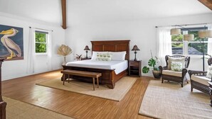 Une chambre spacieuse avec un grand lit, une tête de lit en bois, des tables de chevet, un banc et une chaise.