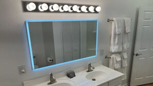 Une salle de bain dotée d’un grand miroir, de deux lavabos et d’un meuble-lavabo avec des tiroirs.