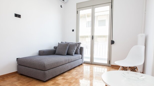 Una sala de estar moderna con un sofá gris, una silla blanca y una mesa con superficie de vidrio.