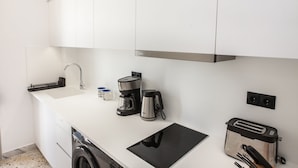 Una cocina moderna con armarios blancos, una campana extractora de acero inoxidable, una cafetera, un hervidor, un tostador y una placa de inducción integrada.