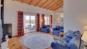 A spacious living area with a wooden ceiling, a large round rug, and blue upholstered furniture. - Vues Spectaculaires sur L'océan.fibre (BORDEIRA)