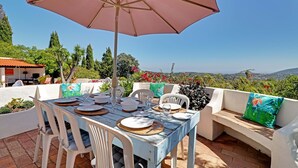 A table set outdoors with a large umbrella, white chairs, and a bench with cushions. - Vues Spectaculaires sur L'océan.fibre (BORDEIRA)