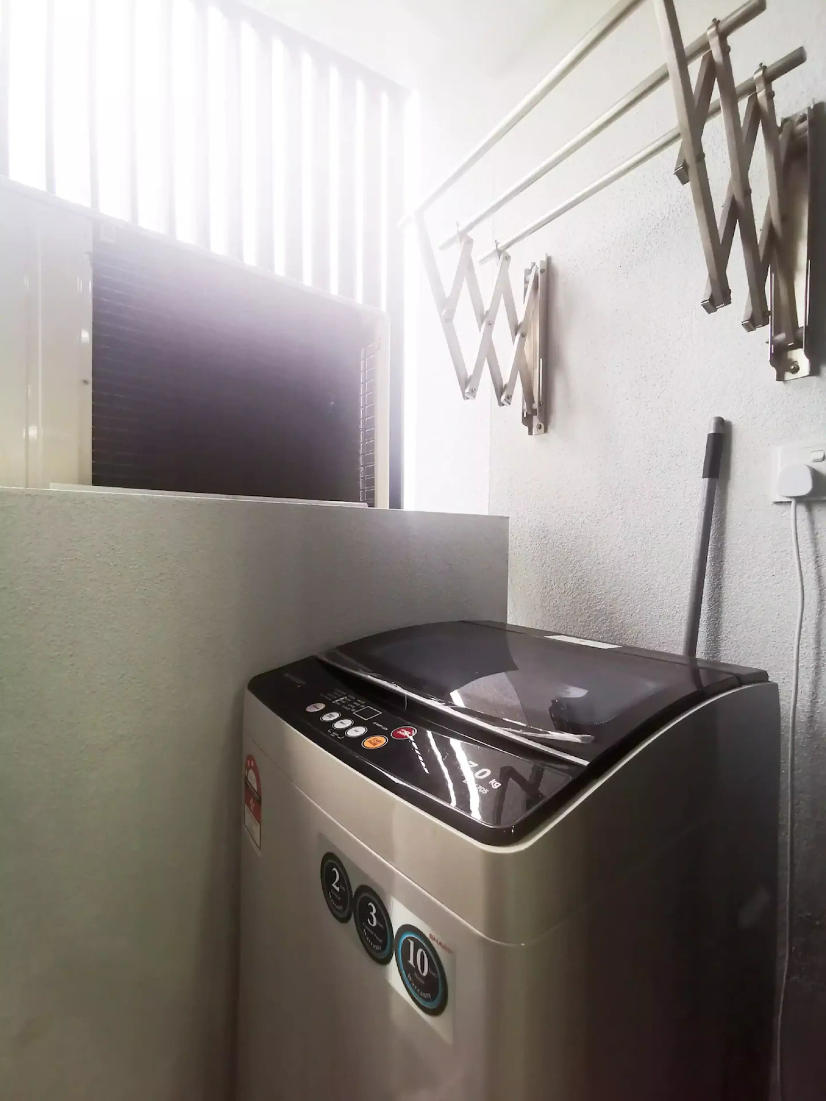 Eine kompakte, edelstahlfarbene Kaffeemaschine mit digitalem Display und mehreren Tasten, in einer Küche mit Fenster und einem Metallregal an der Wand.