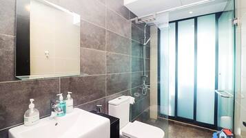 A modern bathroom with a large mirror, a sink with soap dispensers, a toilet, and a glass-enclosed shower area.