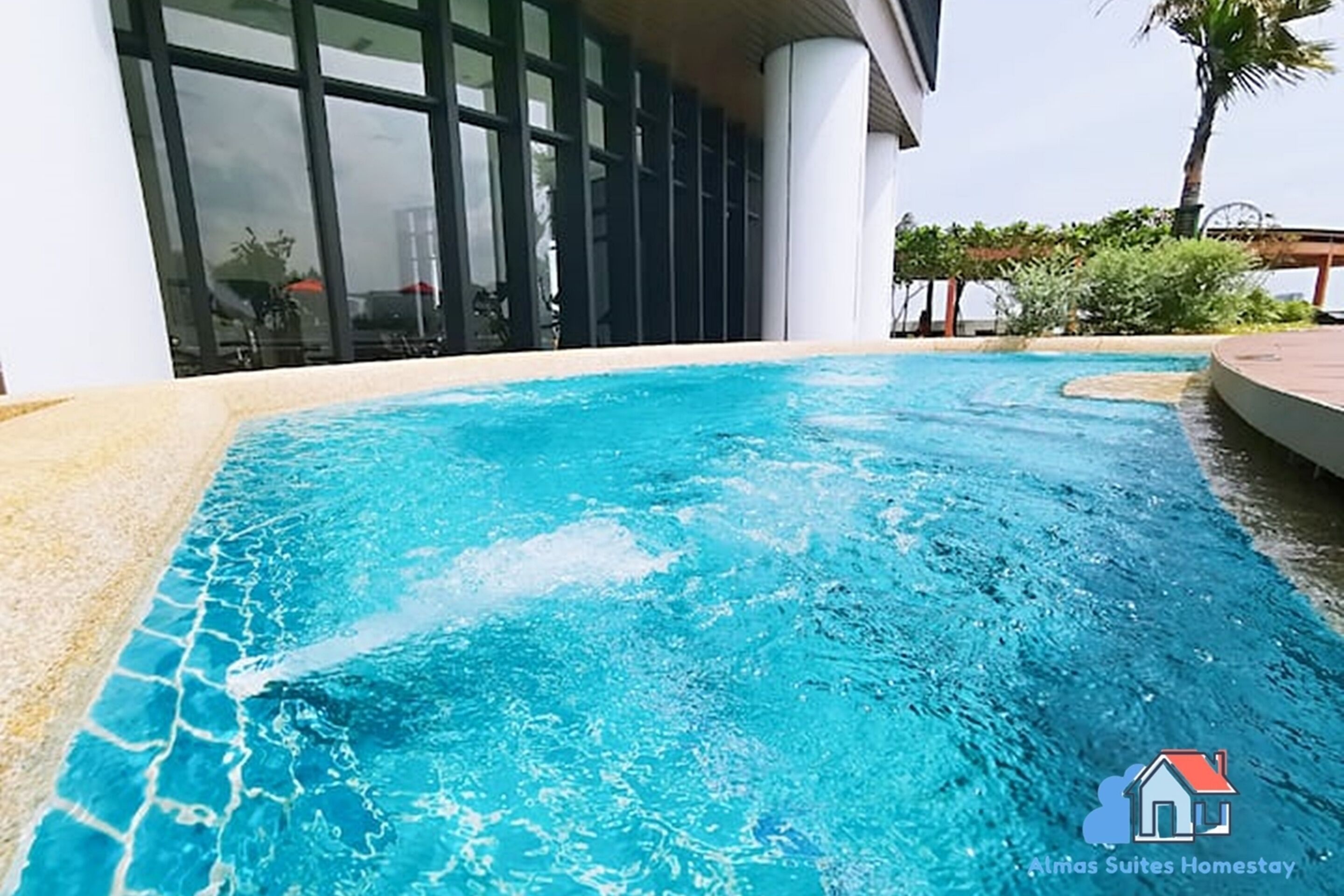 Ein Swimmingpool mit klarem, blauem Wasser, umgeben von einem weißen Gebäude mit großen Fenstern und einer Palme im Hintergrund.
