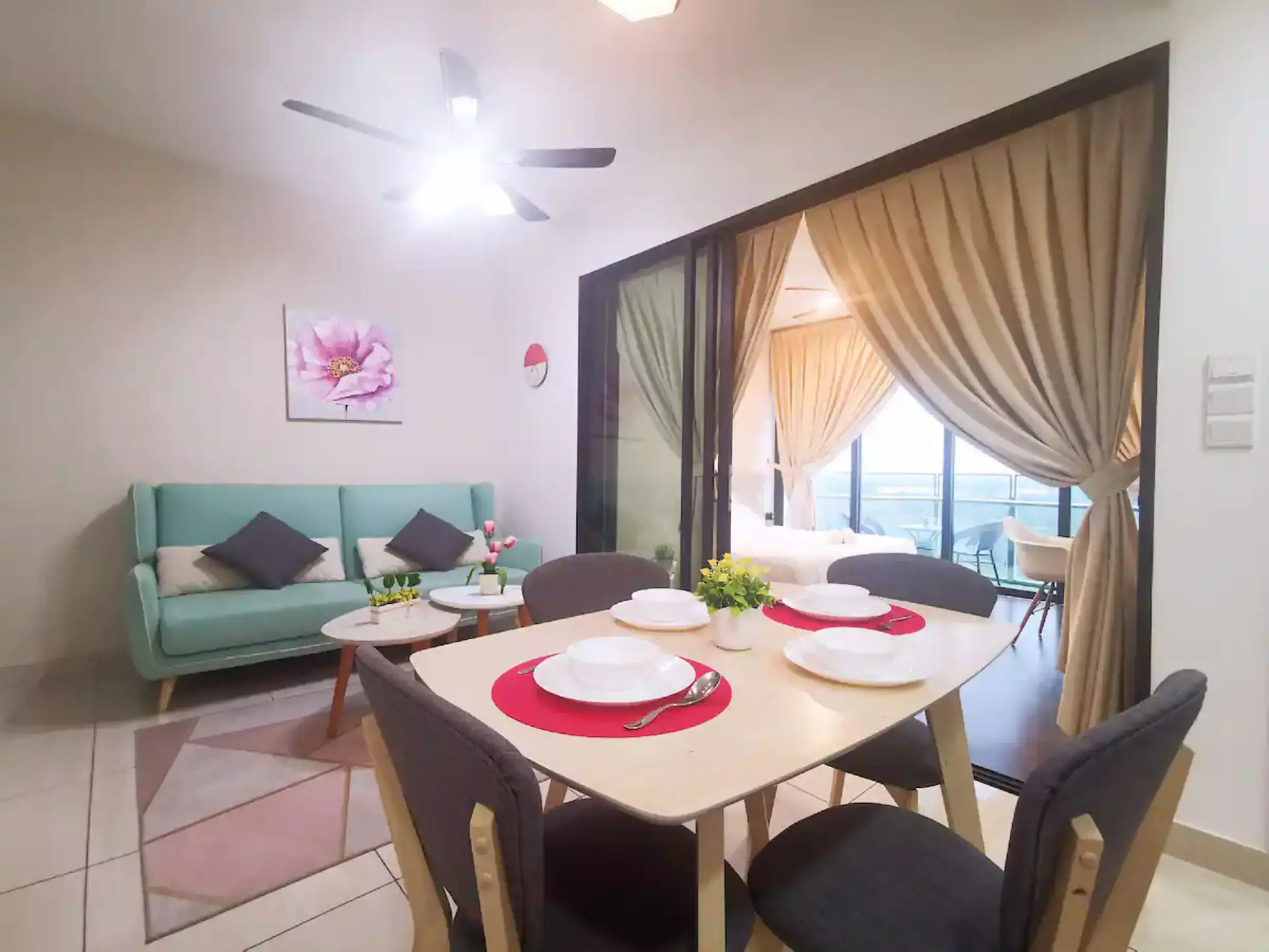 Un coin repas avec une table dressée pour quatre personnes, un canapé, un ventilateur de plafond et une grande fenêtre avec des rideaux.