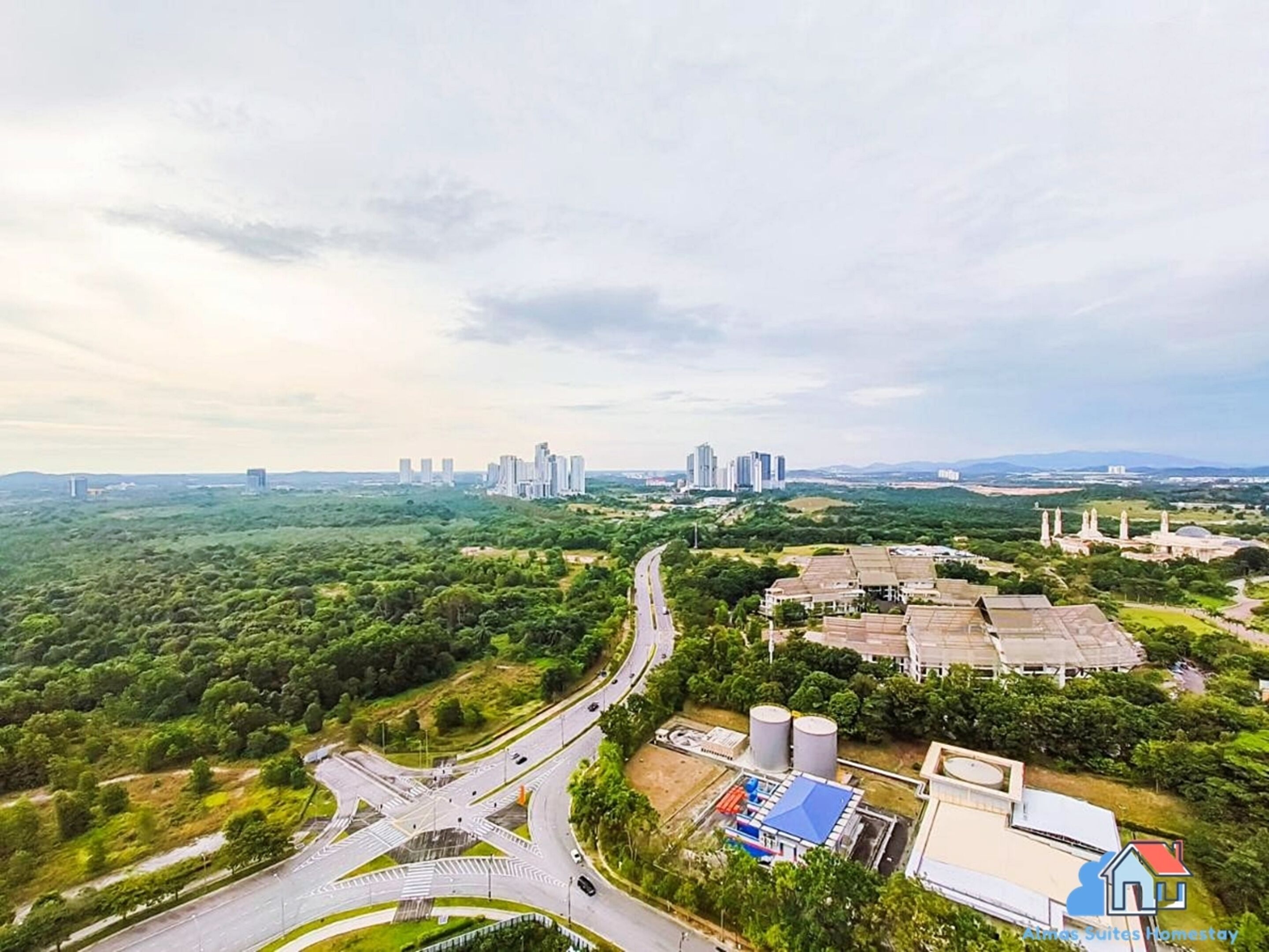 An aerial view of a cityscape with a highway, industrial buildings, and high-rise buildings in the distance.