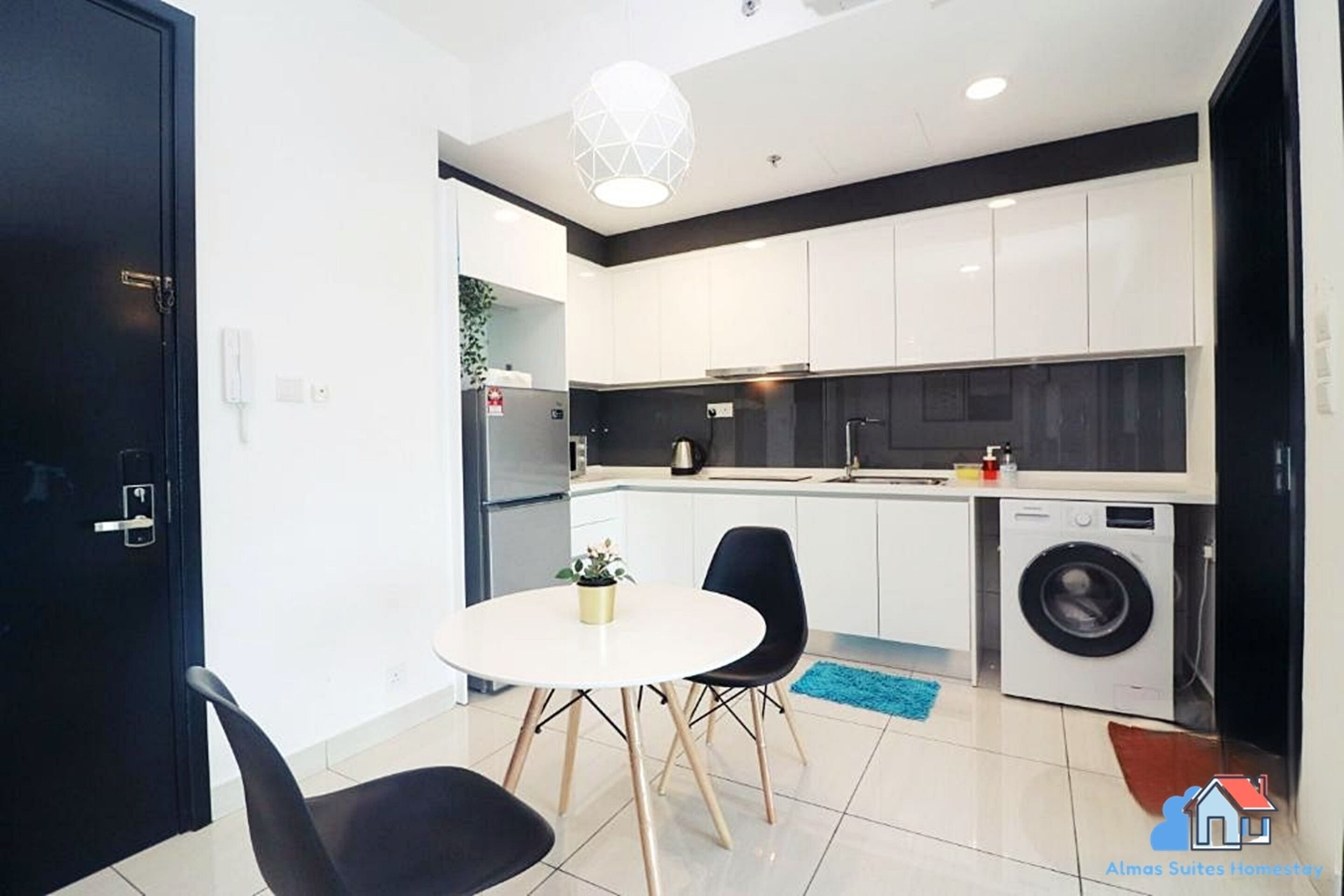 A compact kitchen with white cabinets, a washing machine, and a dining area with a round table and two chairs.