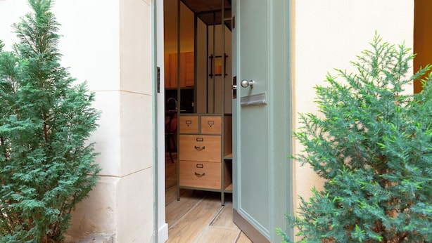 A narrow entrance to a property with a door leading to a room with a bed, a dresser, and a mirror. There are small potted plants on either side of the entrance. - Au pied de la Tour, 1BR/1BA, 4 people (París)