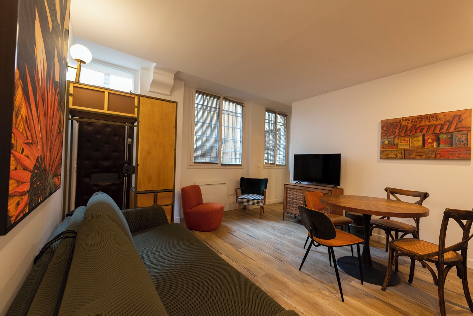 A living room with a sofa, a red chair, a dining table with chairs, a television, and a wall with a colorful artwork.