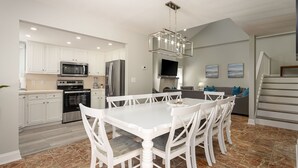 A modern kitchen with white cabinetry, stainless steel appliances, and a dining area with white chairs and a marble floor. - Pet Friendly, Recently Renovated, Private Hot Tub + Free Attraction Tickets! (North Myrtle Beach)