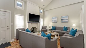 A living room with a fireplace, grey sofas, blue cushions, and a flat-screen TV mounted on the wall. - Pet Friendly, Recently Renovated, Private Hot Tub + Free Attraction Tickets! (North Myrtle Beach)