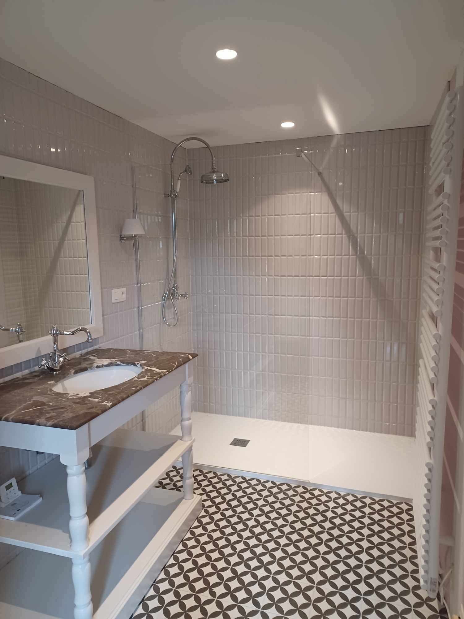 A bathroom with a marble sink, a shower, and patterned floor tiles.
