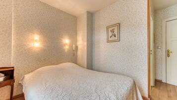 Ein Schlafzimmer mit einem großen Bett, floralem Wandpapier, Wandleuchten und einer Tür rechts.