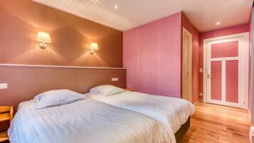 A room with two beds, wooden flooring, a pink wall, and a white door.
