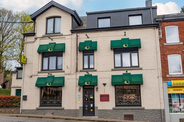 A building with multiple windows, green awnings, and a black door. - Hôtel Le Cor de Chasse (Saint-Hubert)