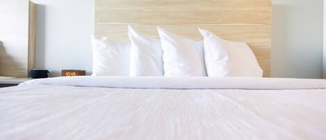 A neatly made bed with white linens and pillows, a wooden headboard, and a digital clock displaying the time.
