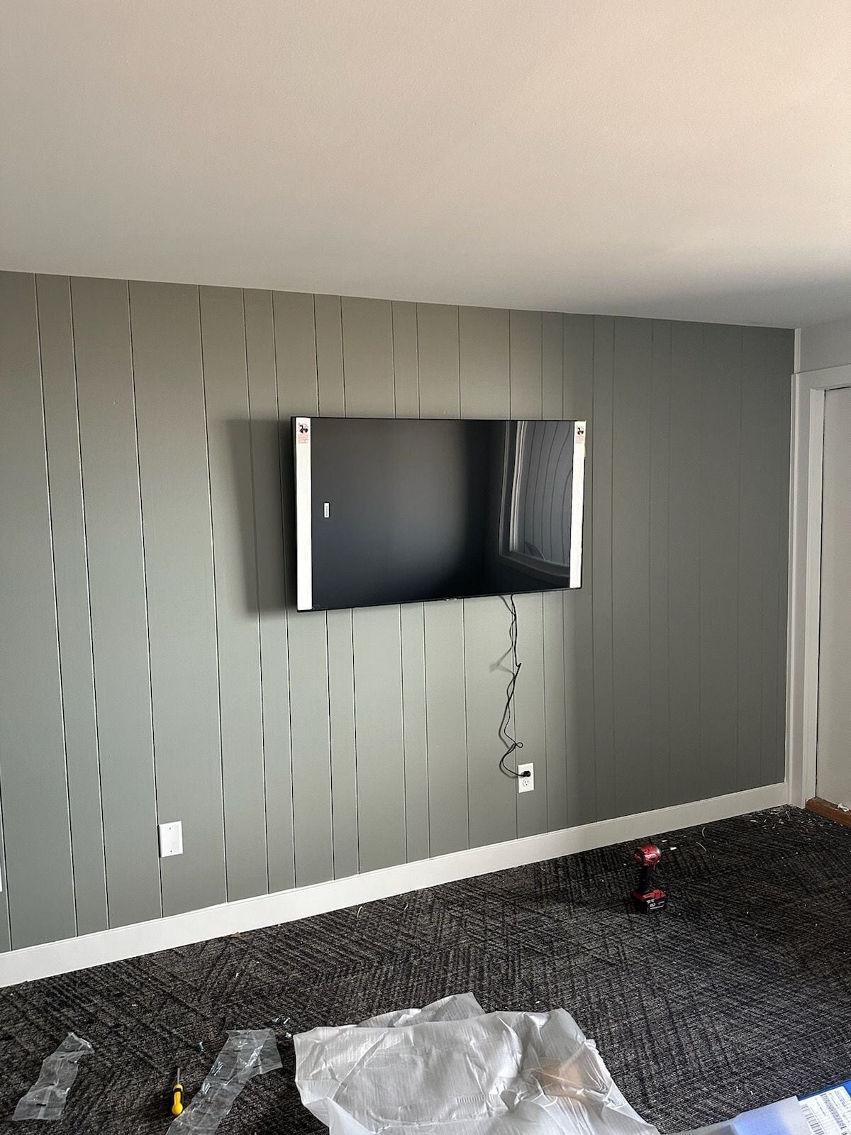 Una habitación con un televisor montado en una pared gris, suelo alfombrado y zócalo blanco.