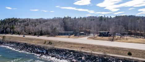 A coastal road with a rocky shoreline, a forested hill in the background, and a clear sky.