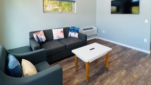 Una sala de estar moderna con un sofá gris, una mesa de centro blanca y un televisor de pantalla plana montado en la pared.